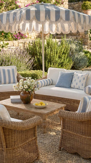 Outdoor patio setting with striped umbrella, wicker furniture, and a small table with flowers and fruit.