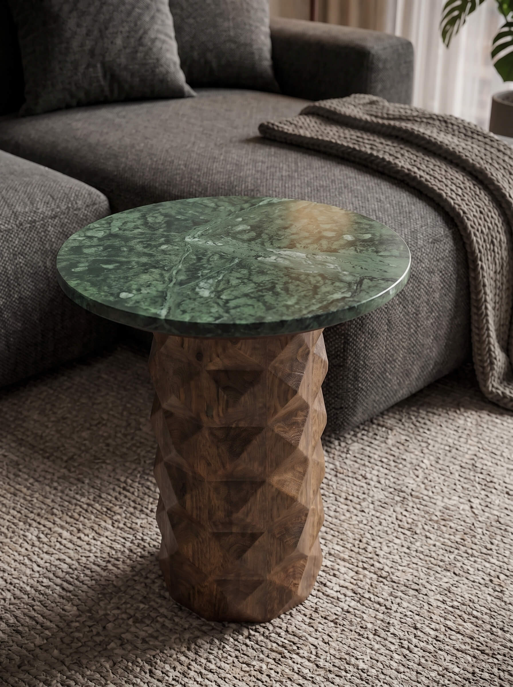 A round side table with a green marbled top and a textured, faceted brown wooden pedestal base, styled in a living room next to a gray sofa.