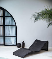 Black wicker lounge chair in a room with a large arched window and a plant.