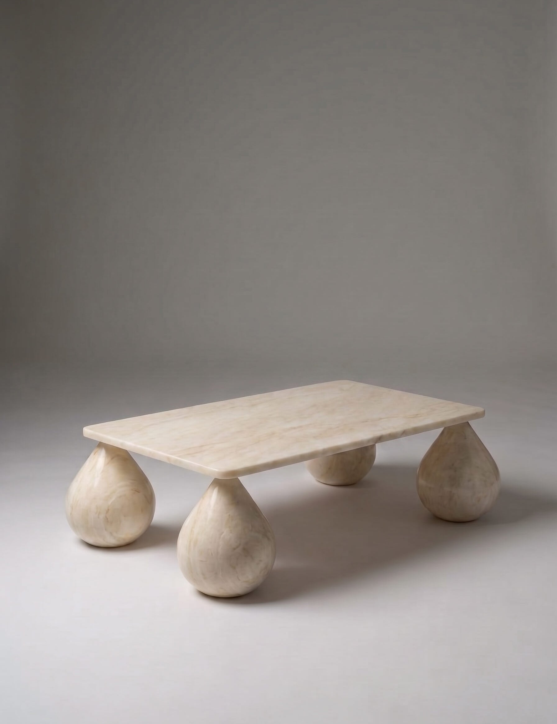A low rectangular stone coffee table with rounded teardrop-shaped legs, made from a light beige natural stone, photographed on a neutral gray studio background.
