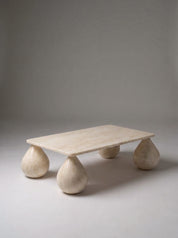 A low rectangular stone coffee table with rounded teardrop-shaped legs, made from a light beige natural stone, photographed on a neutral gray studio background.