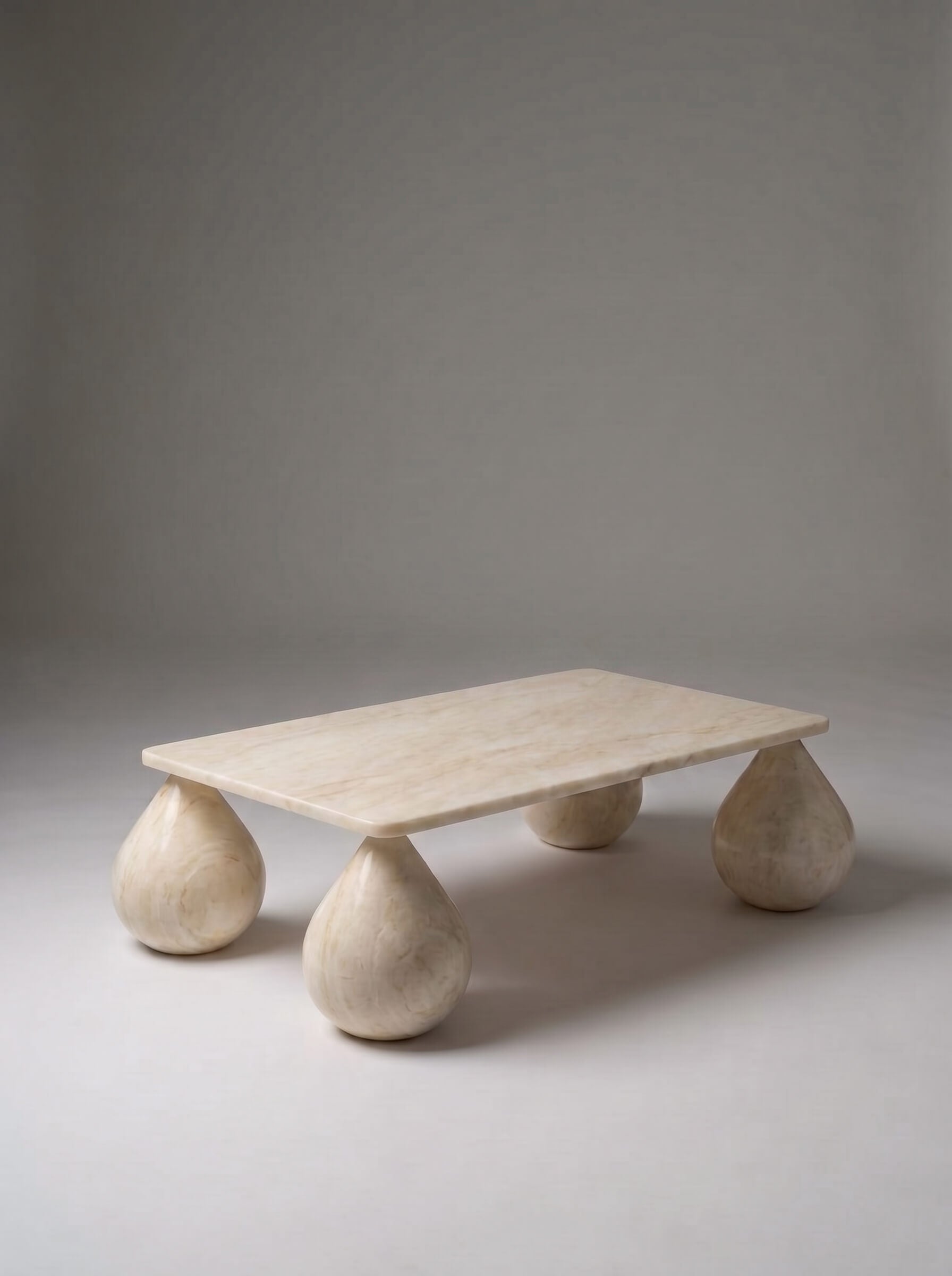 A low rectangular stone coffee table with rounded teardrop-shaped legs, made from a light beige natural stone, photographed on a neutral gray studio background.