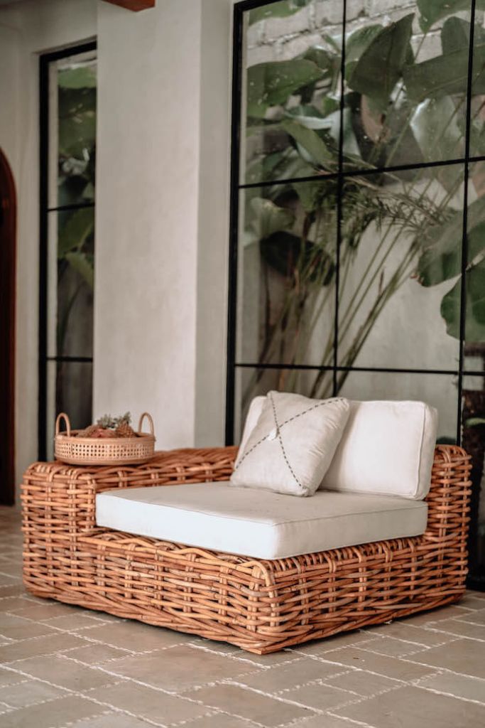 Wicker outdoor sofa with cushions against a glass wall with greenery