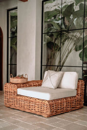 Wicker outdoor sofa with cushions against a glass wall with greenery