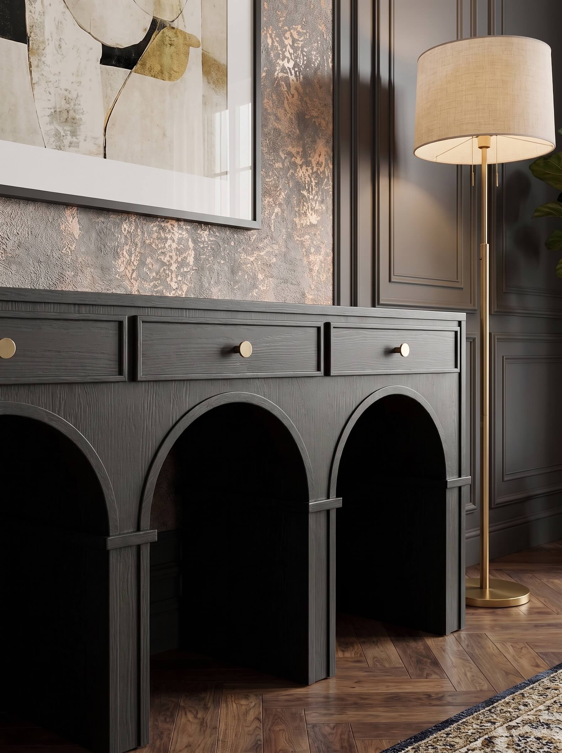 A dark charcoal gray console table with three arched legs and three drawers, styled in a luxury room next to a gold floor lamp.