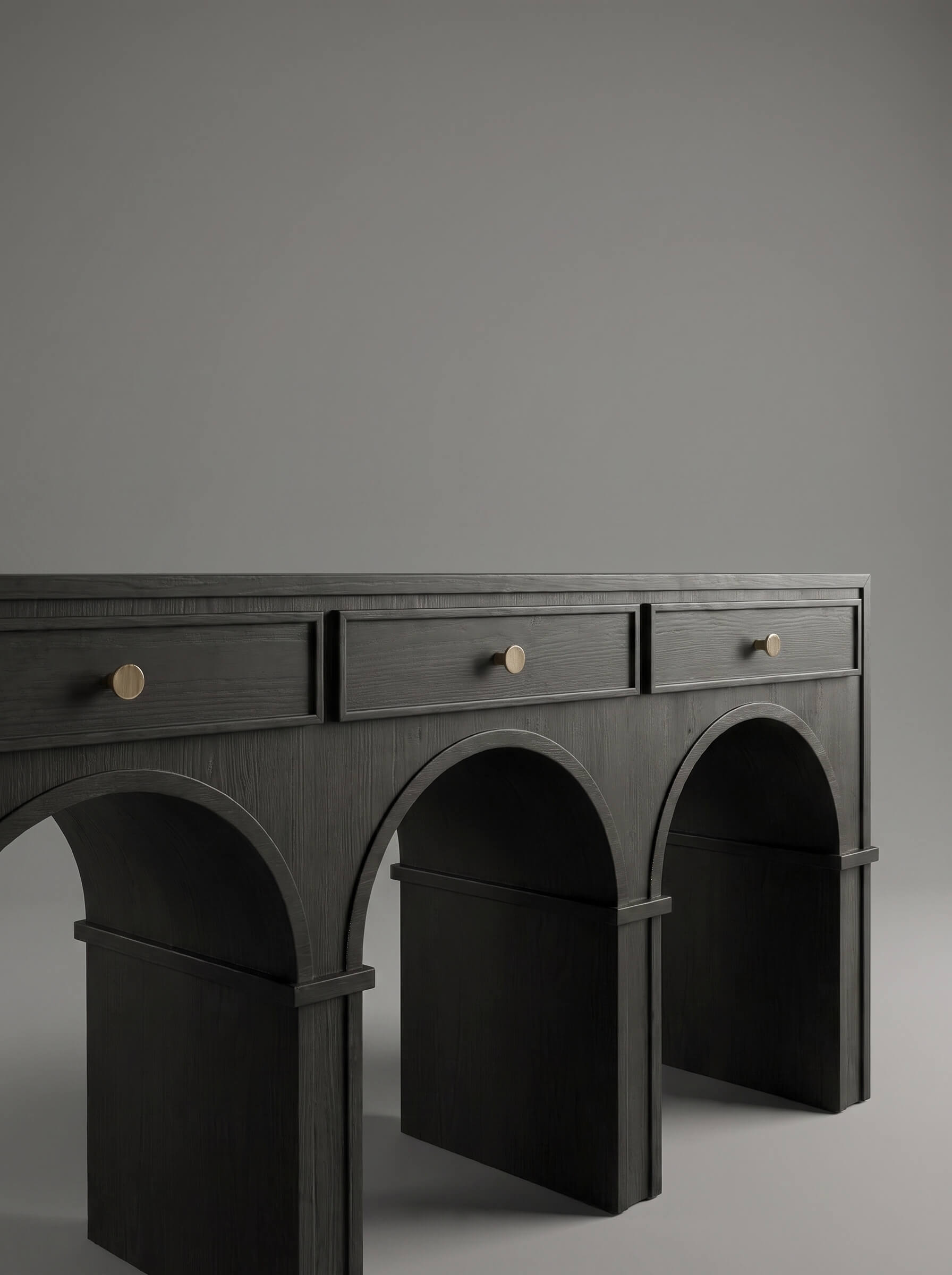 A dark charcoal gray console table with three drawers and three arched legs, featuring small round brass knobs, set against a solid gray studio background.