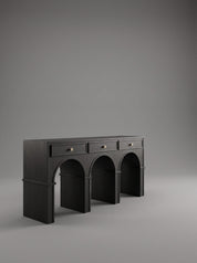 A black wooden console table with three drawers on top and three arched legs underneath, shown against a neutral gray studio background.
