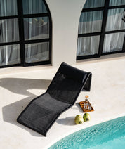 Black lounge chair by a pool with a tray of drinks and fruits