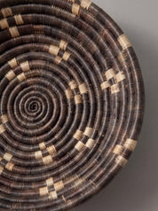 A close-up of a hand-woven spiral basket with concentric rings in dark brown and natural tan.