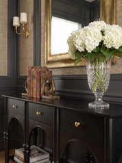 Black wood console table with three drawers, triple-arch apron, and brass-capped legs, styled beneath a round mirror