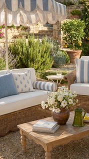 Outdoor seating area with wicker furniture, striped canopy, and a wooden table with flowers and books.