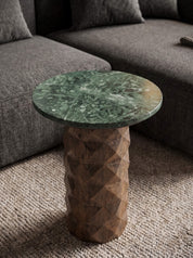 A round side table with a green marble top and a faceted wooden pedestal base, styled in a living room setting next to a gray sofa.