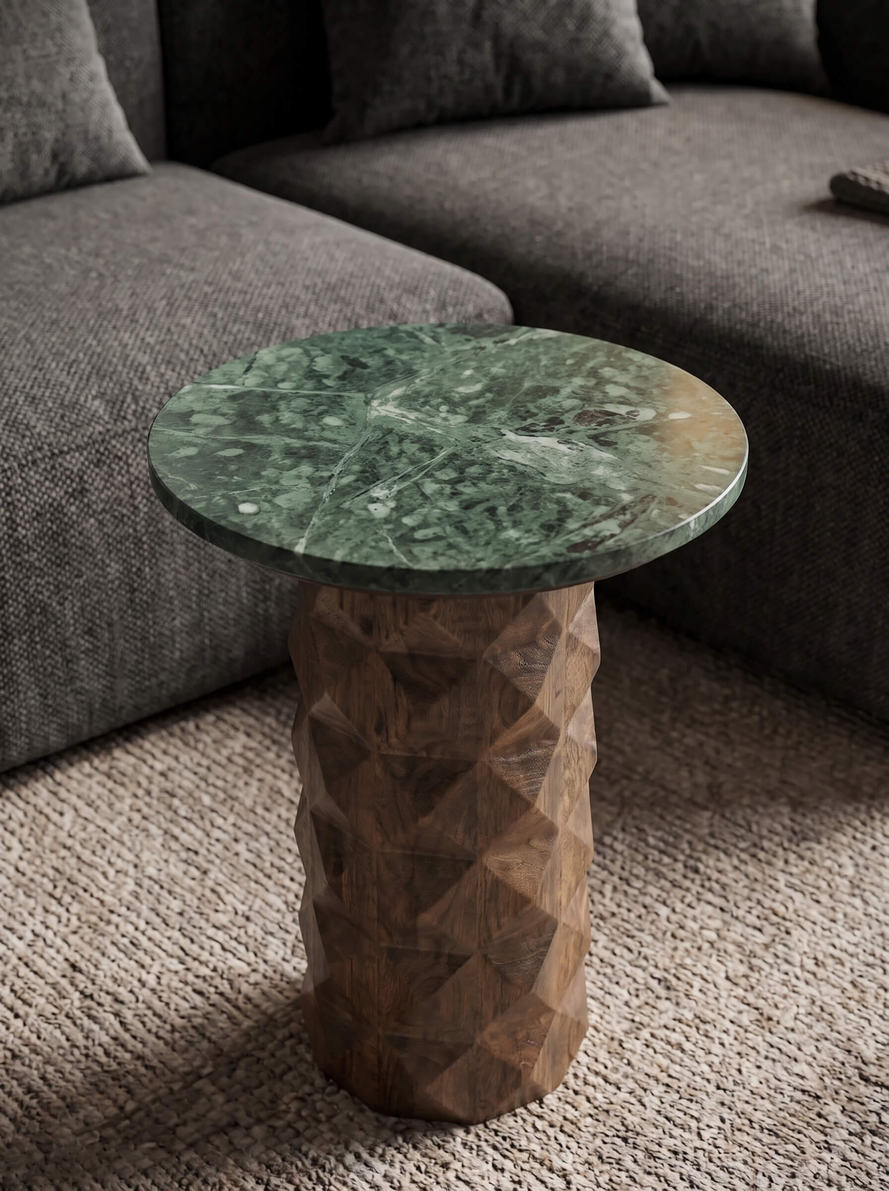 A round side table with a green marble top and a faceted wooden pedestal base, styled in a living room setting next to a gray sofa.