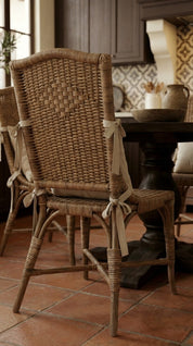 Wicker chair with a woven backrest on a terracotta tiled floor in a kitchen setting.