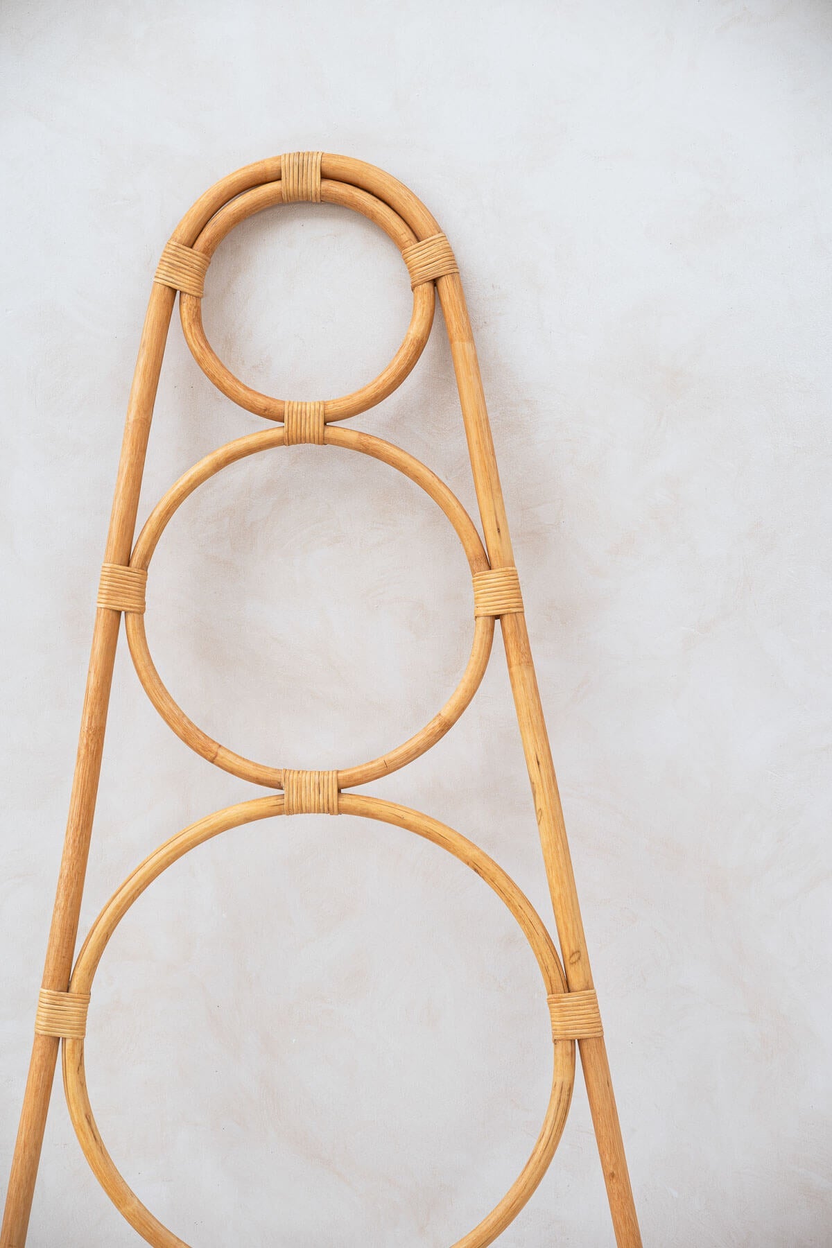 Rattan plant stand with circular design on a light gray background