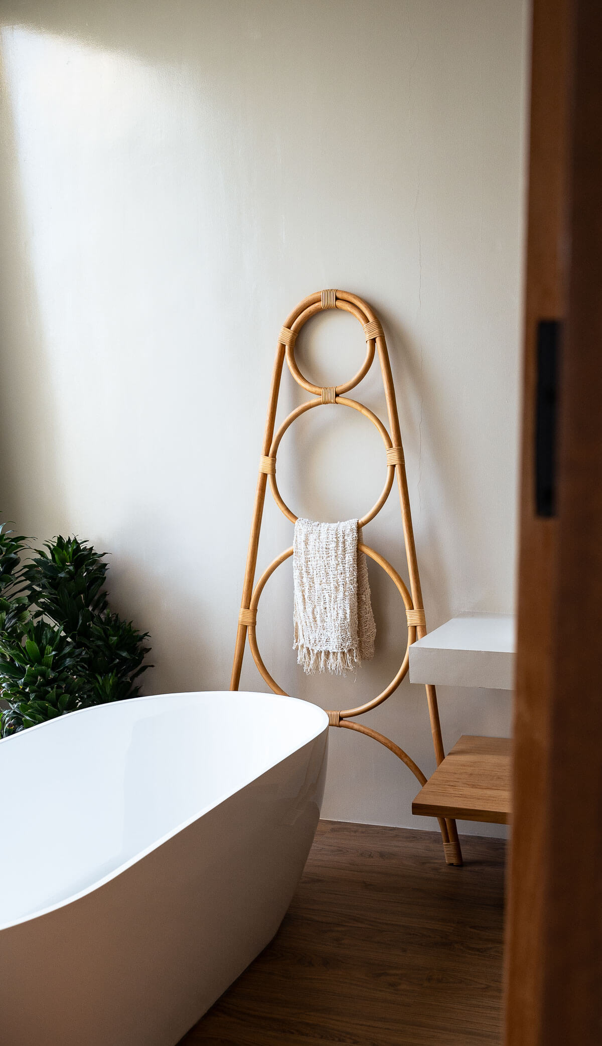 Bathroom with a freestanding bathtub, wooden towel rack, and plant.