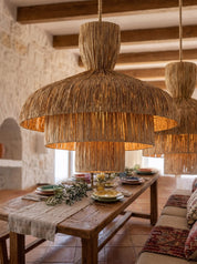 Large woven straw pendant lights hanging over a rustic wooden dining table in a warm, stone-walled room.