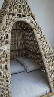 Wicker chair with a cushioned seat and backrest against a plain wall.