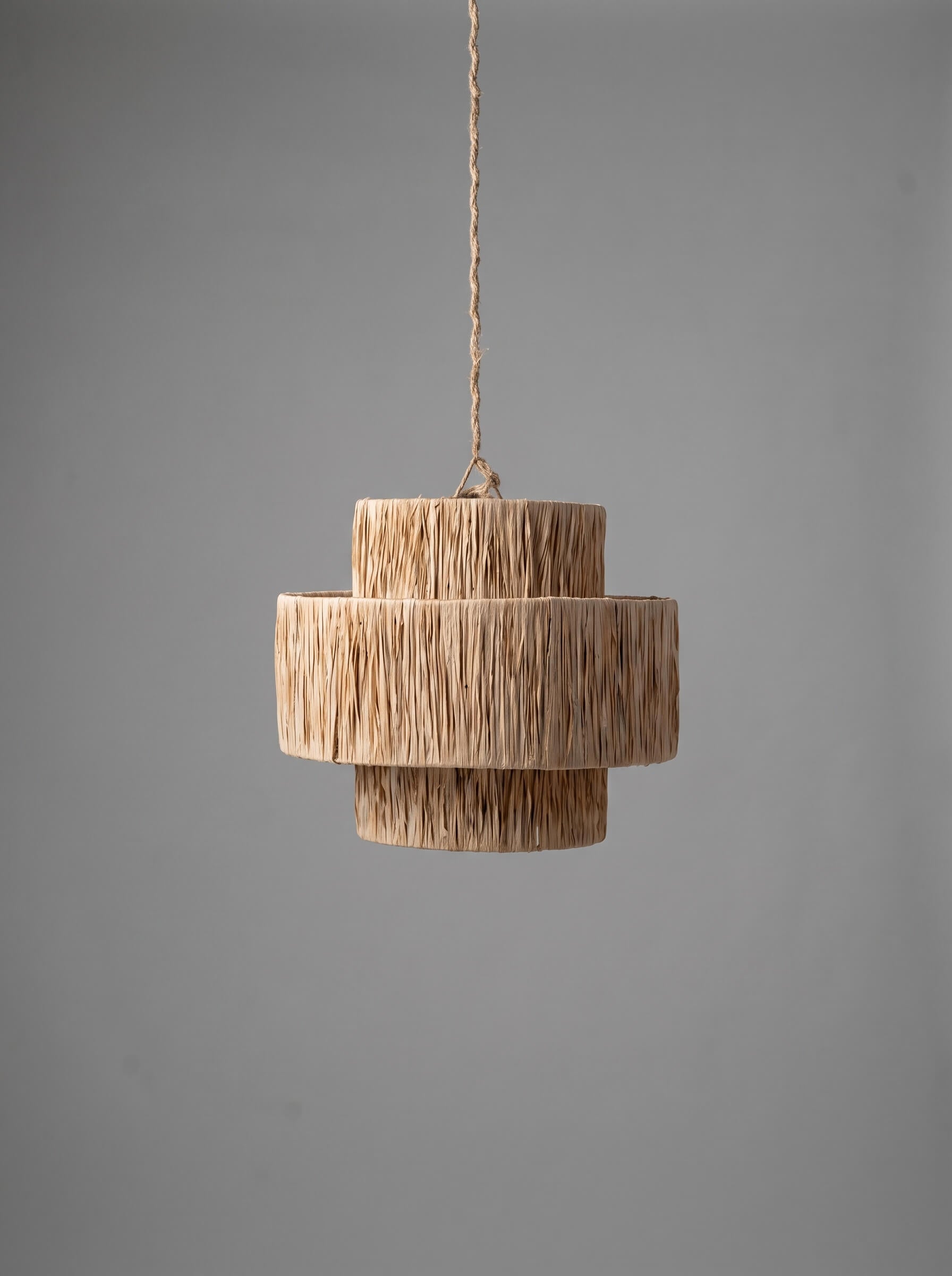 A modern three-tiered pendant light with a textured, woven natural fiber shade, suspended by a thin cord against a solid gray background.