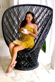 Woman in a yellow dress sitting in a black wicker chair holding a cup and saucer.