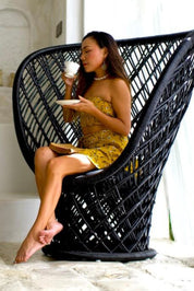 Woman in a yellow dress sitting in a black wicker chair holding a cup.