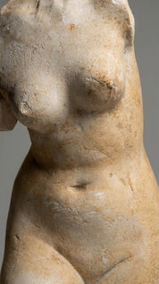 Stone sculpture of a female figure from the waist up against a gray background