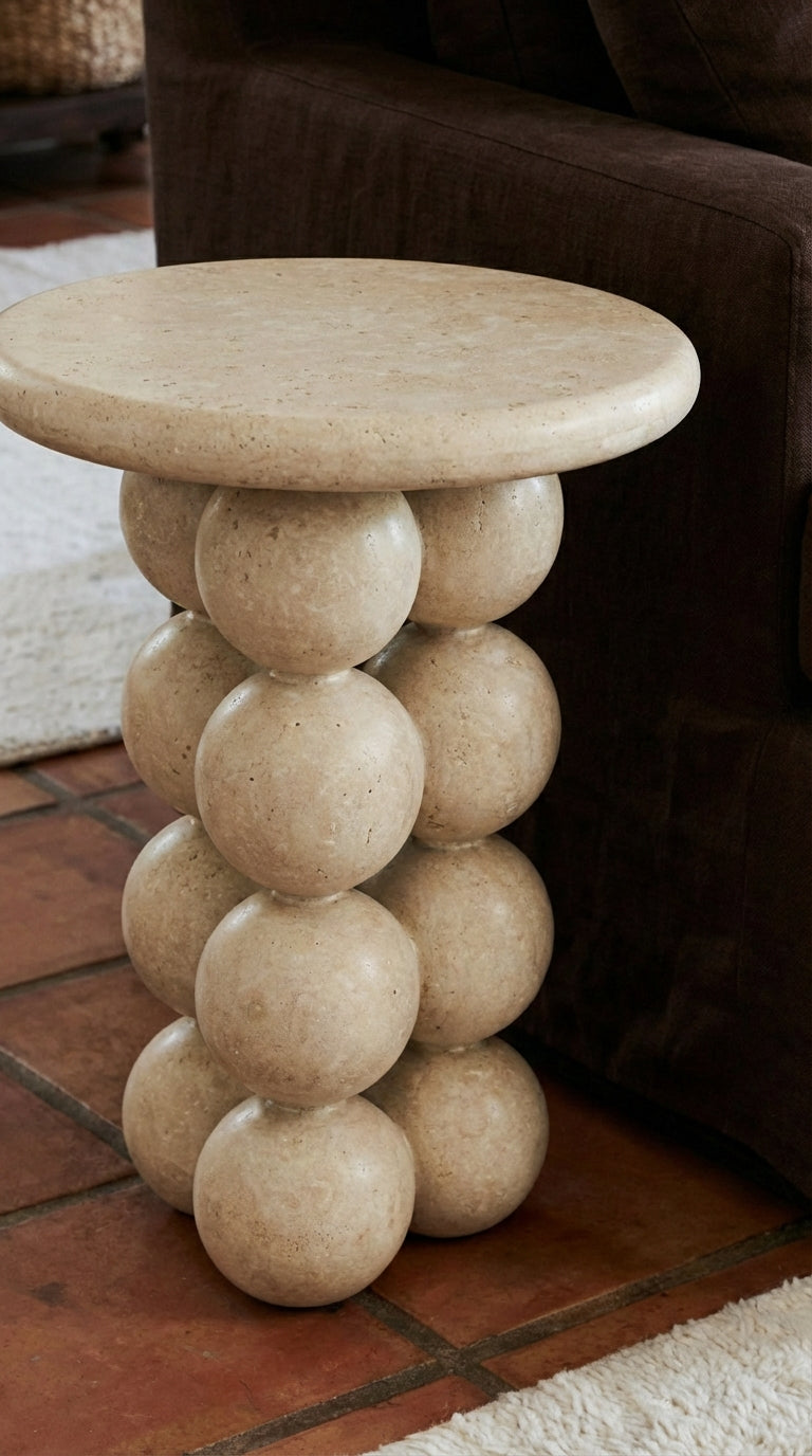 Round stone side table with spherical design on a tiled floor.