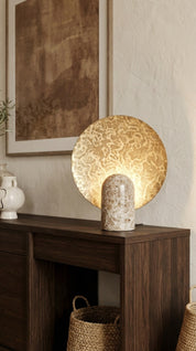 Decorative lamp on a wooden console table with a textured wall and framed art in the background.