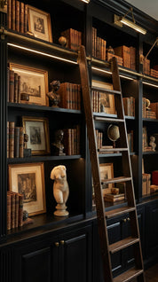 Dark wooden bookshelf with books, framed pictures, and decorative items, featuring a wooden ladder.