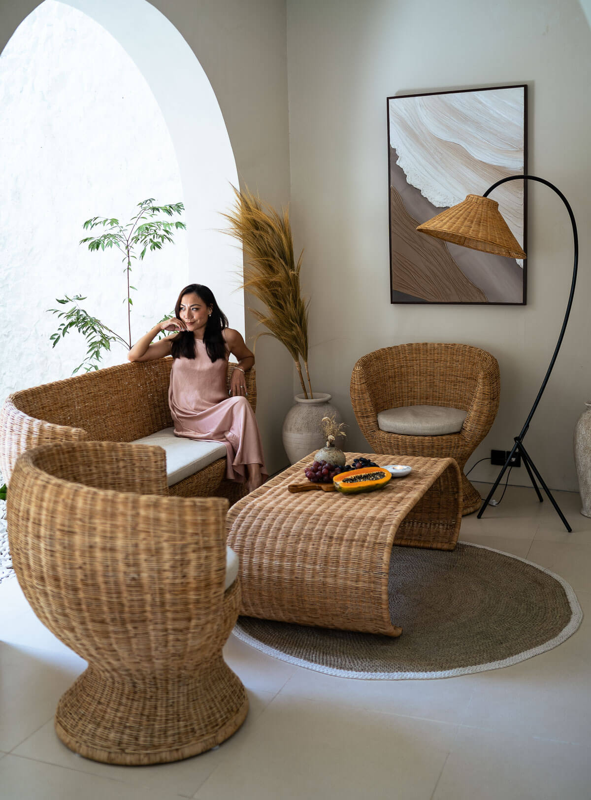 Woman sitting in a modern living room with wicker furniture and decor.