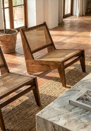 Wooden chairs with woven backrests on a patio with a marble table and plant in the background.