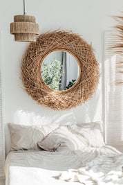 Woven mirror on a wall above a bed with white bedding