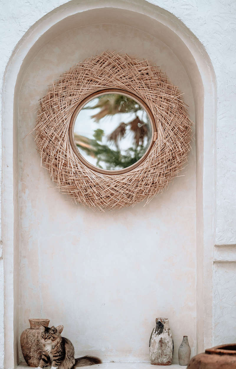 Round woven mirror on a white wall with decorative vases below.