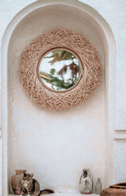 Round woven mirror on a white wall with decorative vases below.