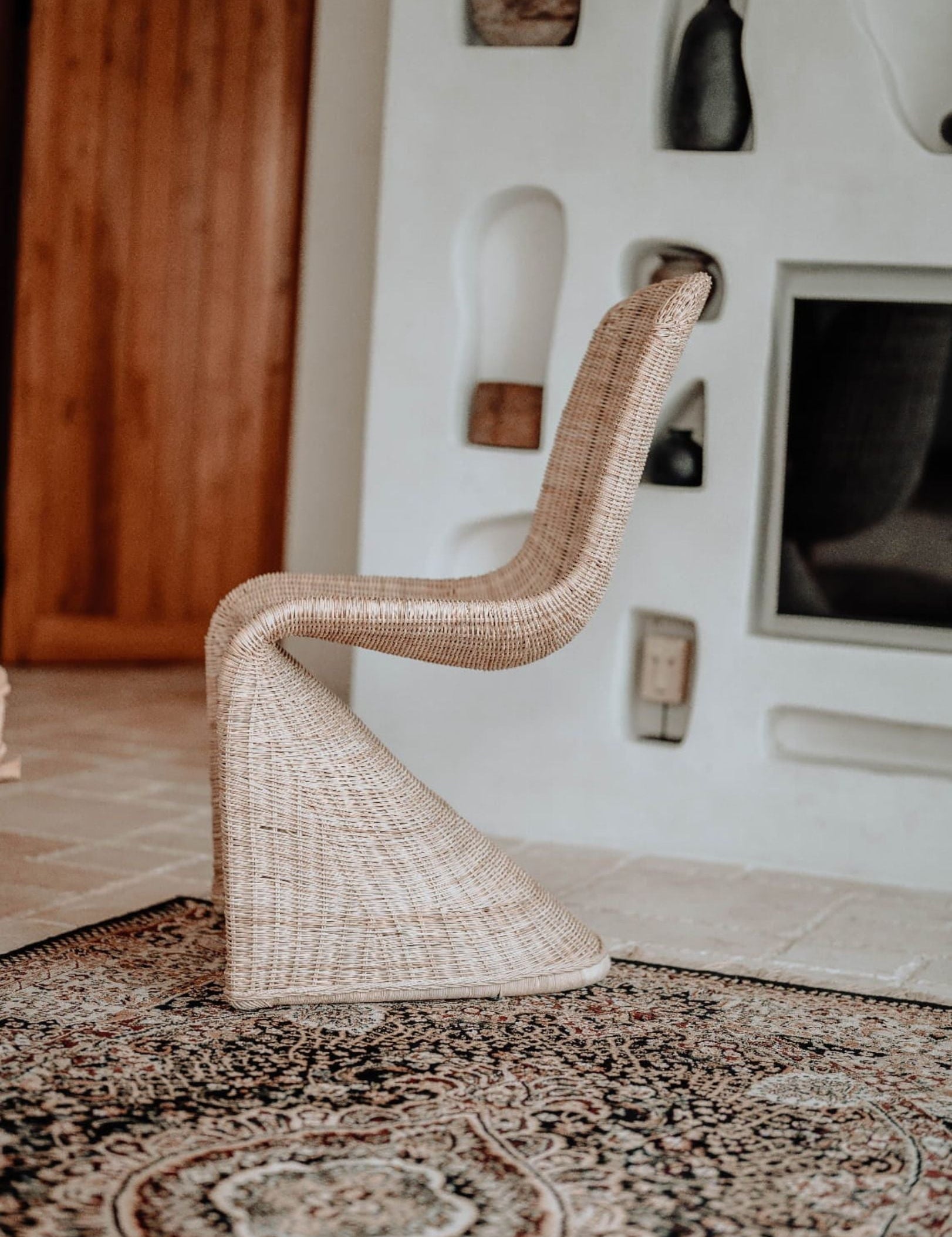 Woven chair on a patterned rug with a textured wall in the background
