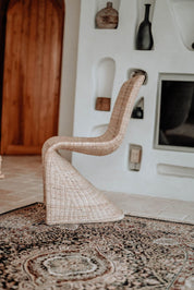 Woven chair on a patterned rug with a textured wall in the background