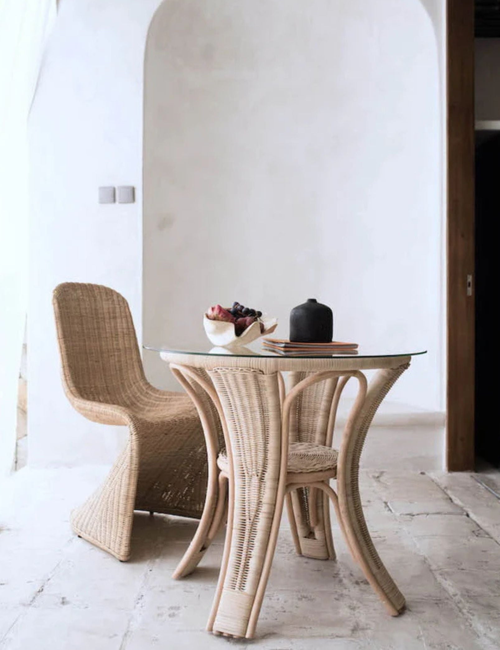 Oriana Ori round rattan table with woven shelf and braided legs, topped with thick glass, showcasing handcrafted natural rattan design and artisanal details