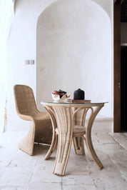 Oriana Ori round rattan table with woven shelf and braided legs, topped with thick glass, showcasing handcrafted natural rattan design and artisanal details