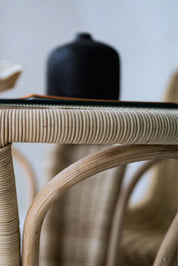 Oriana Ori round rattan table with woven shelf and braided legs, topped with thick glass, showcasing handcrafted natural rattan design and artisanal details