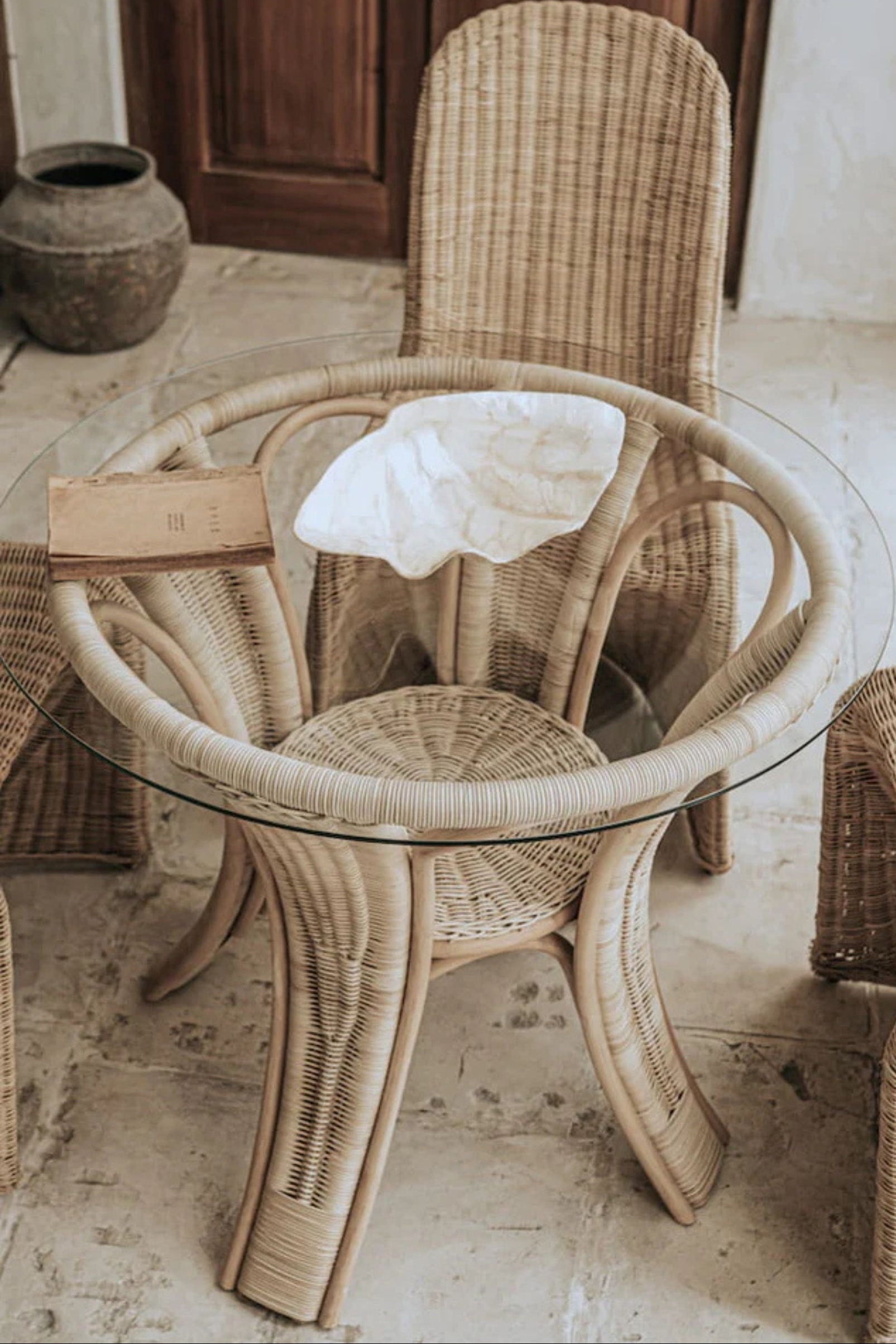 Oriana Ori round rattan table with woven shelf and braided legs, topped with thick glass, showcasing handcrafted natural rattan design and artisanal details