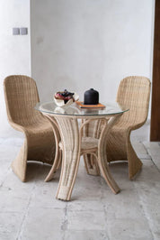 Oriana Ori round rattan table with woven shelf and braided legs, topped with thick glass, showcasing handcrafted natural rattan design and artisanal details