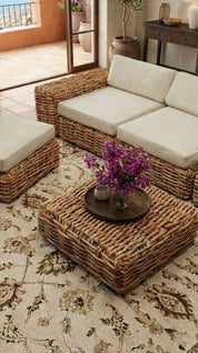 Modern living room with rattan furniture, a fireplace, and large windows overlooking a scenic view.