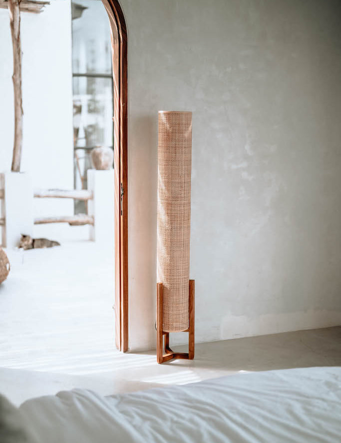 Tall wooden floor lamp against a white wall in a minimalistic room.