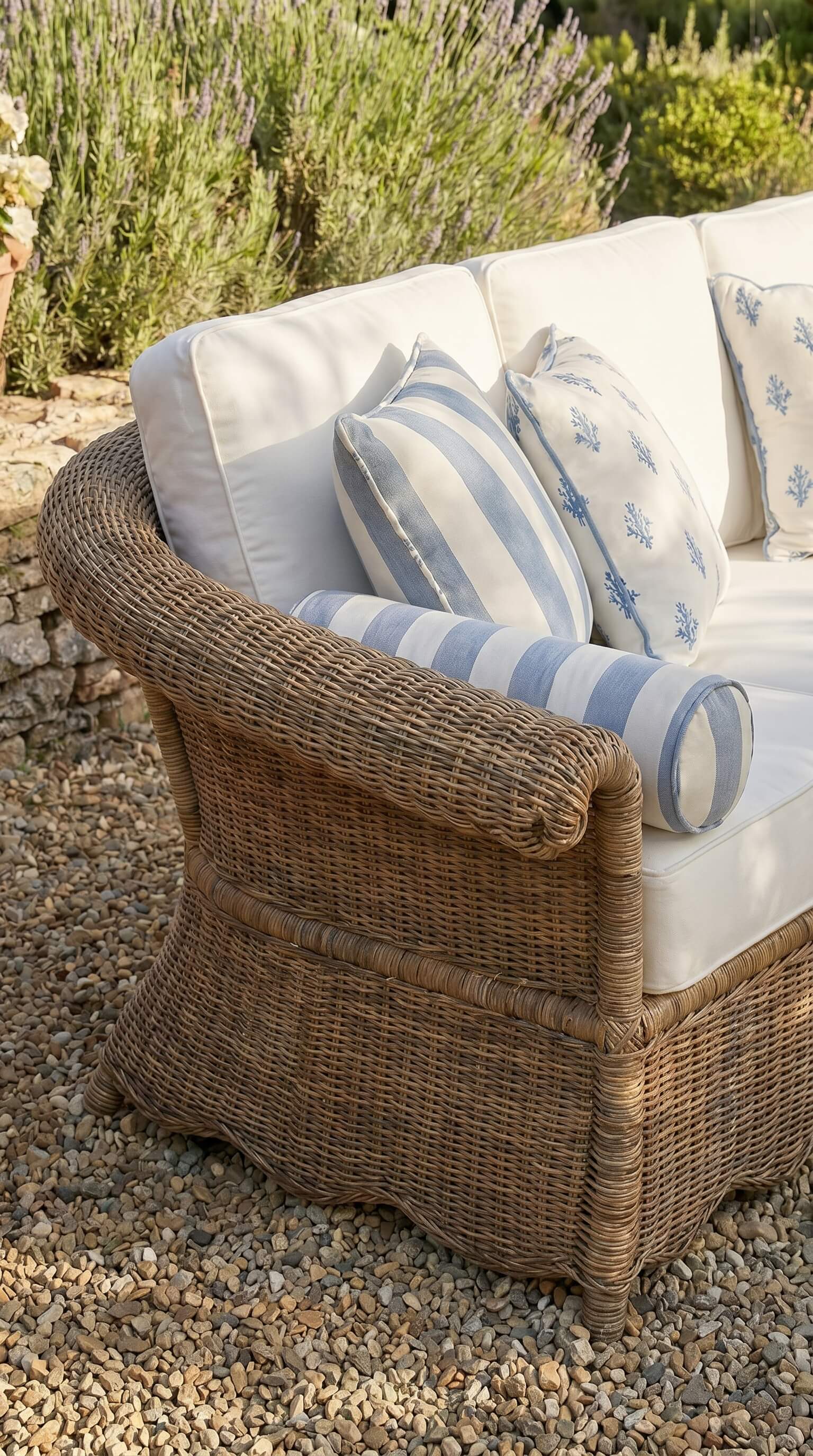 Wicker chair with cushions on a gravel surface with plants in the background