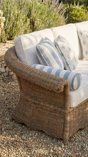 Wicker chair with cushions on a gravel surface with plants in the background
