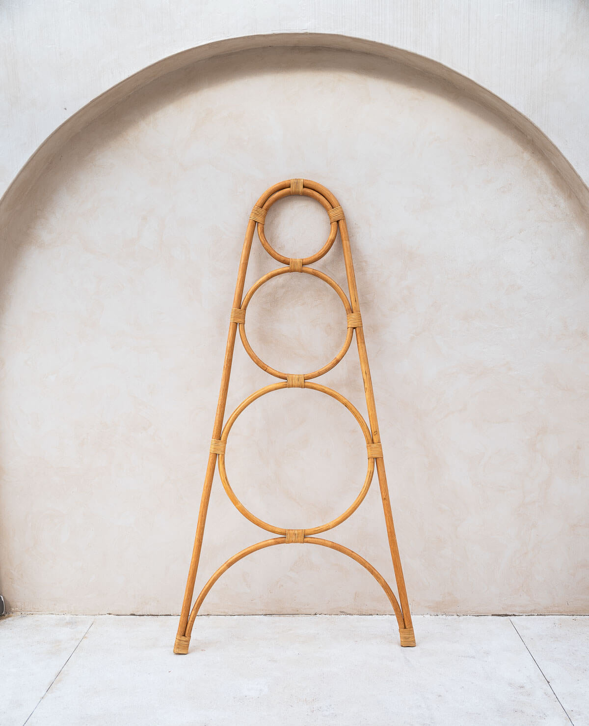 Rattan plant stand with circular design against a light wall.