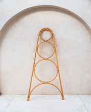 Rattan plant stand with circular design against a light wall.
