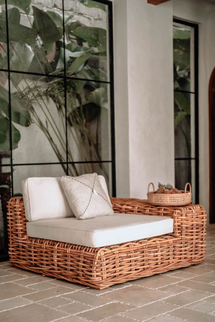 Wicker outdoor furniture set with cushions against a wall with large glass panels.
