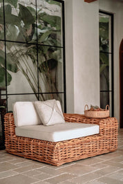 Wicker outdoor furniture set with cushions against a wall with large glass panels.