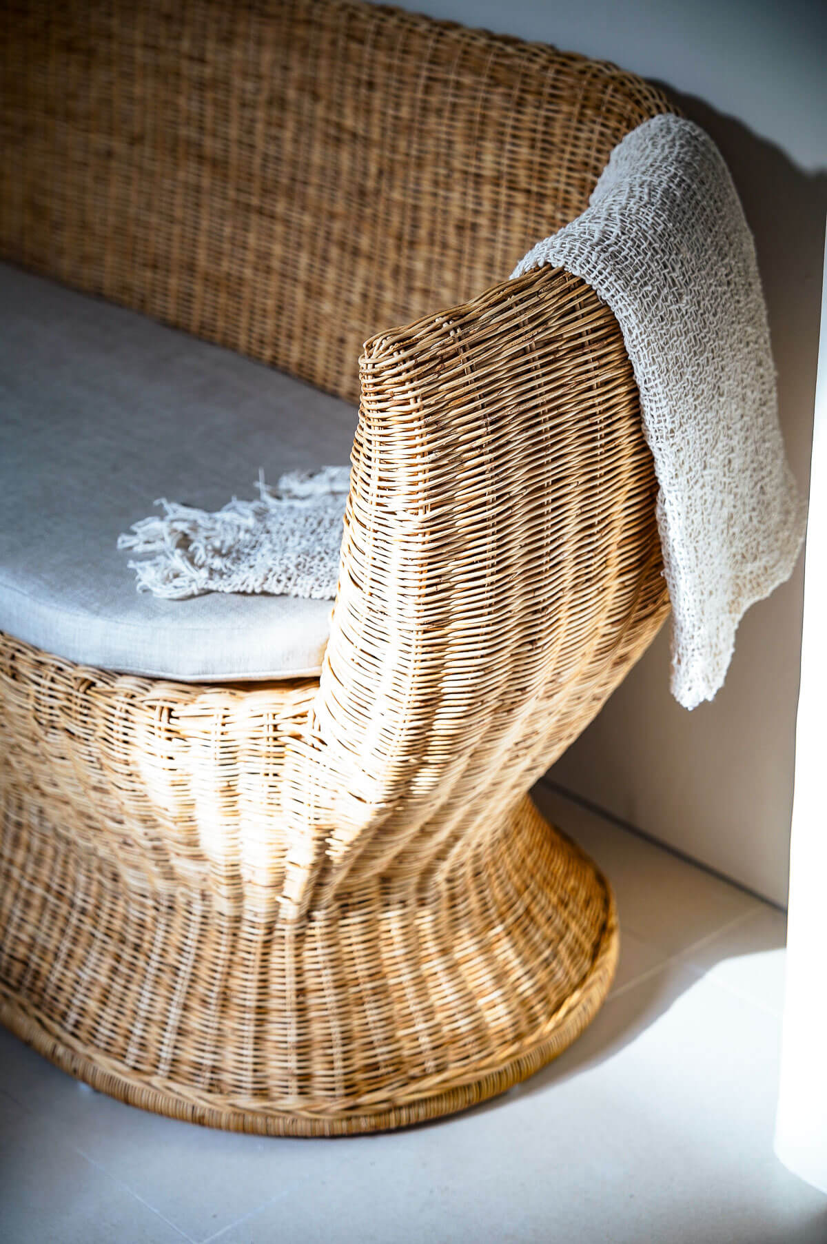 Wicker chair with a textured cushion and white blanket on a light gray floor.